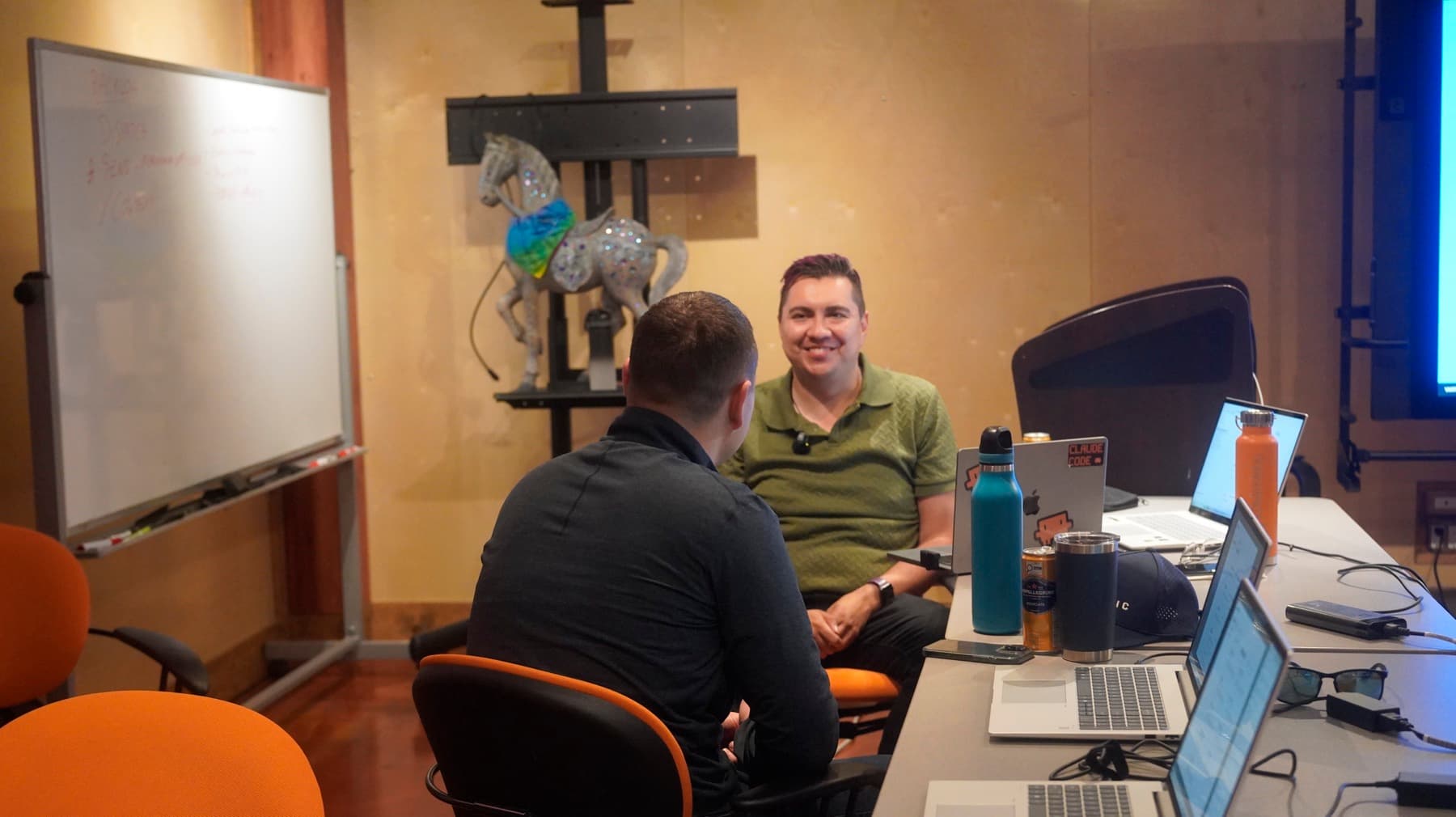 Instructor seated at a table with laptops, talking with an attendee seen from behind